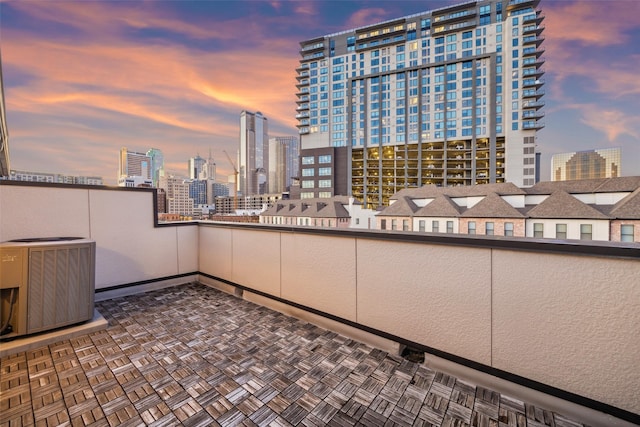 patio terrace at dusk featuring central AC unit and a balcony