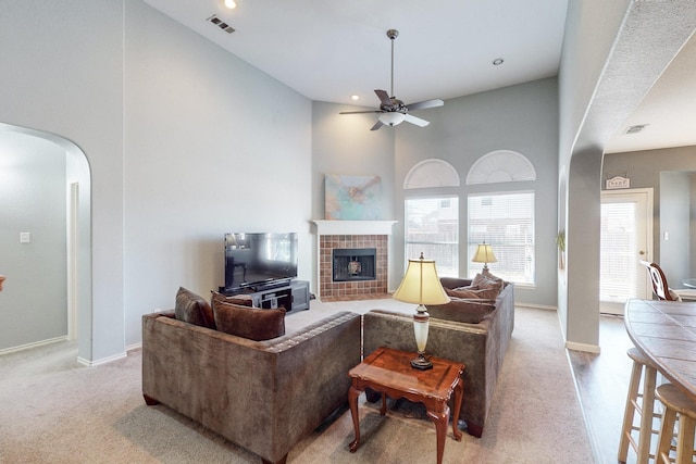 carpeted living room featuring a tiled fireplace, ceiling fan, and a high ceiling