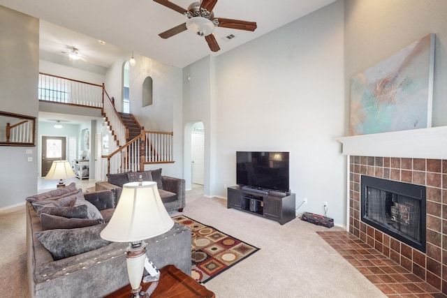 carpeted living room with ceiling fan, a towering ceiling, and a fireplace