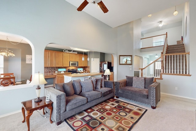 living room featuring a towering ceiling, ceiling fan with notable chandelier, and light carpet