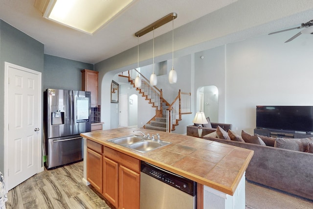 kitchen with appliances with stainless steel finishes, sink, hanging light fixtures, a center island with sink, and light hardwood / wood-style flooring