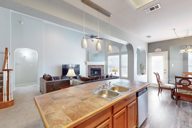 kitchen with sink, hanging light fixtures, tile counters, a fireplace, and stainless steel dishwasher