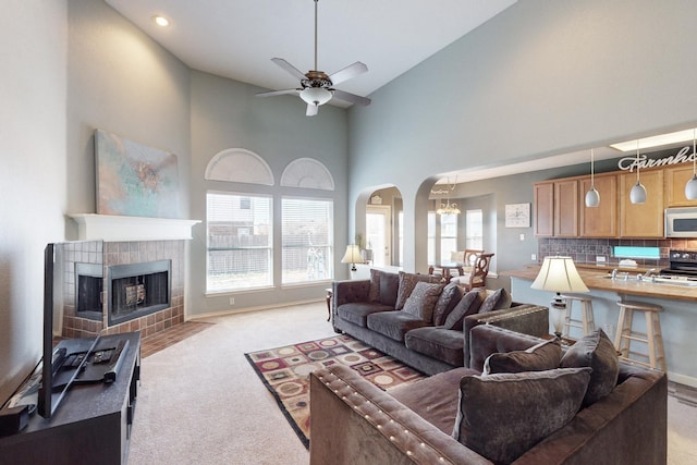 carpeted living room featuring high vaulted ceiling, a tile fireplace, and ceiling fan