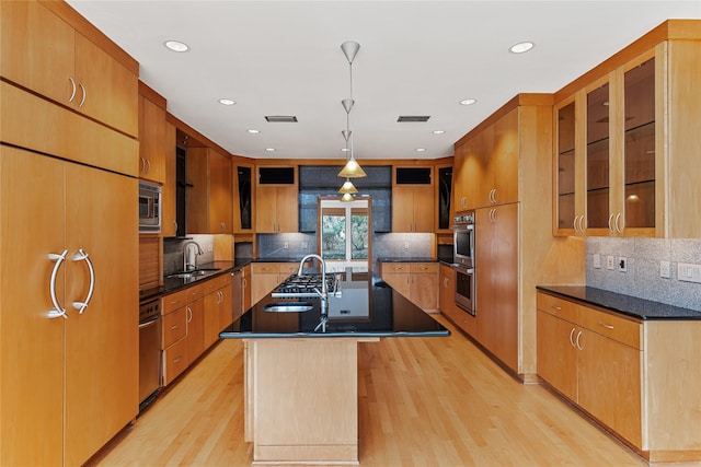 kitchen with stainless steel appliances, a kitchen island with sink, light hardwood / wood-style floors, and decorative light fixtures