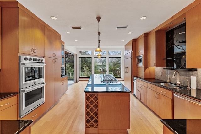 kitchen featuring a kitchen island, decorative light fixtures, sink, built in appliances, and light wood-type flooring