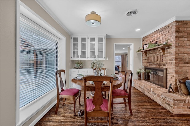 dining space with a brick fireplace, crown molding, and dark wood-type flooring