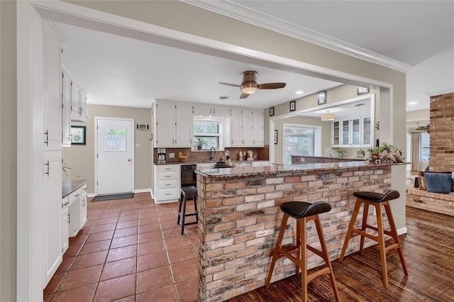 kitchen with stone counters, a breakfast bar, white cabinetry, backsplash, and kitchen peninsula