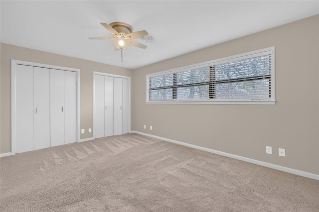 unfurnished bedroom with multiple closets, carpet flooring, and ceiling fan