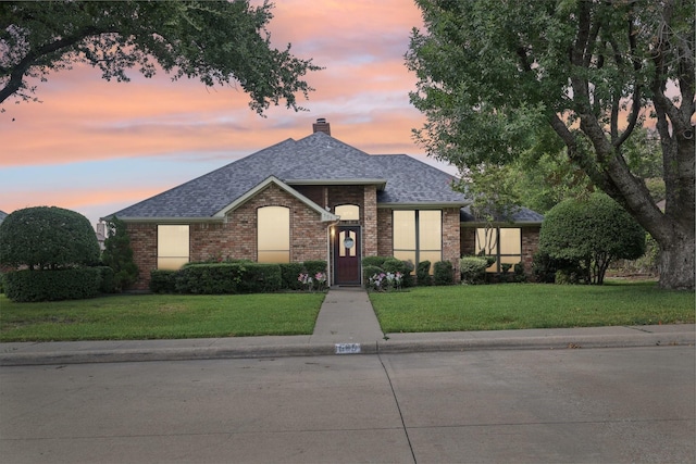 view of front of house with a yard, brick siding, and a shingled roof