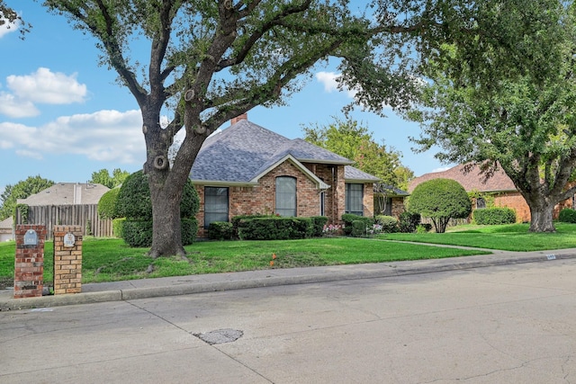 view of front of home featuring brick siding, a front yard, roof with shingles, and fence