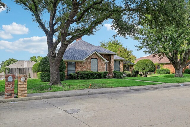 view of front of home featuring brick siding, a front yard, roof with shingles, and fence