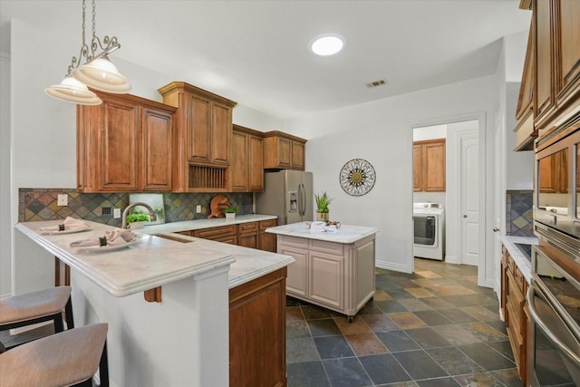 kitchen with a breakfast bar area, appliances with stainless steel finishes, a kitchen island, washer / dryer, and kitchen peninsula