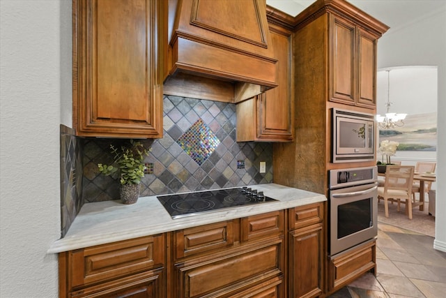 kitchen featuring decorative backsplash, custom exhaust hood, a notable chandelier, stainless steel appliances, and light stone countertops