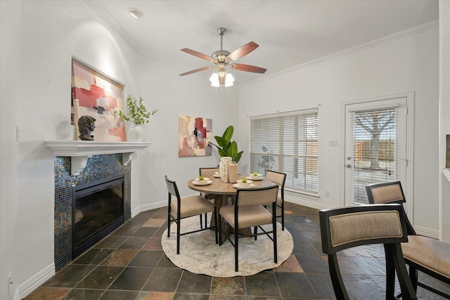 dining area with a tiled fireplace, ornamental molding, and ceiling fan