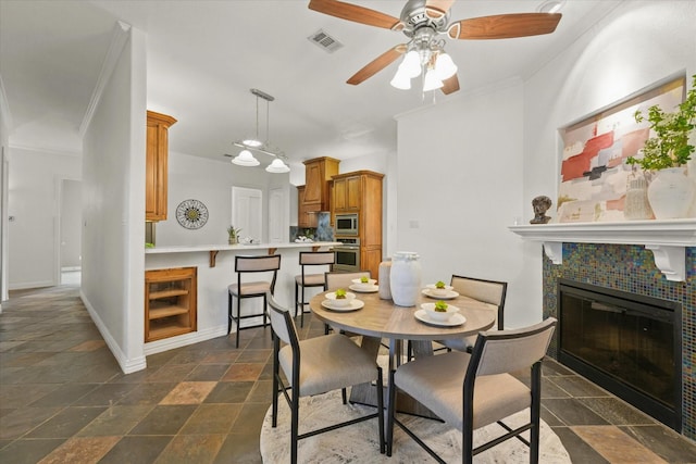 dining area with ceiling fan, ornamental molding, and a tile fireplace