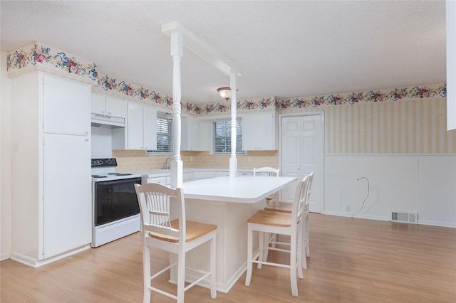 kitchen with light hardwood / wood-style flooring, a kitchen bar, white range with electric stovetop, white cabinets, and a kitchen island