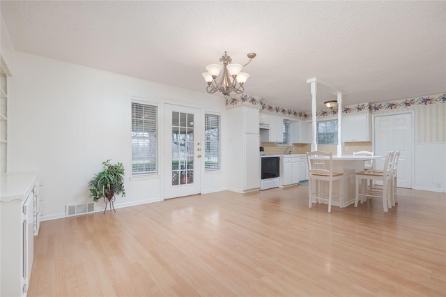 unfurnished dining area with an inviting chandelier, a textured ceiling, and light wood-type flooring