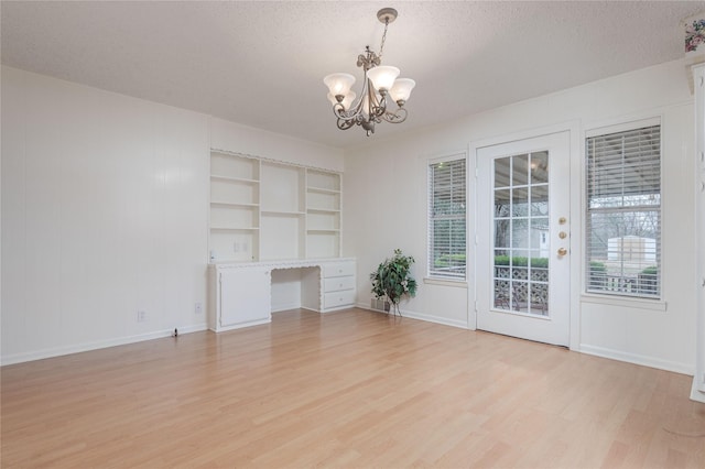 unfurnished living room with a notable chandelier, light hardwood / wood-style flooring, and a textured ceiling