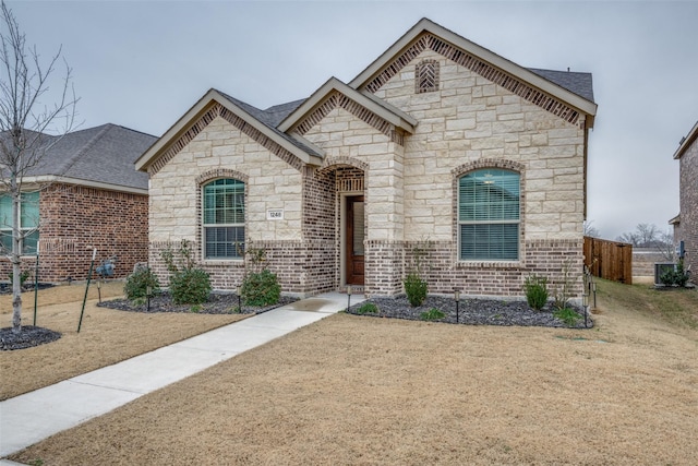 french country home featuring fence, a front lawn, and brick siding