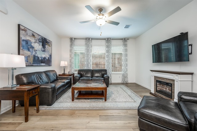 living room featuring a ceiling fan, baseboards, visible vents, light wood-style floors, and a glass covered fireplace