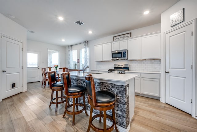 kitchen featuring a center island with sink, stainless steel appliances, light countertops, visible vents, and decorative backsplash