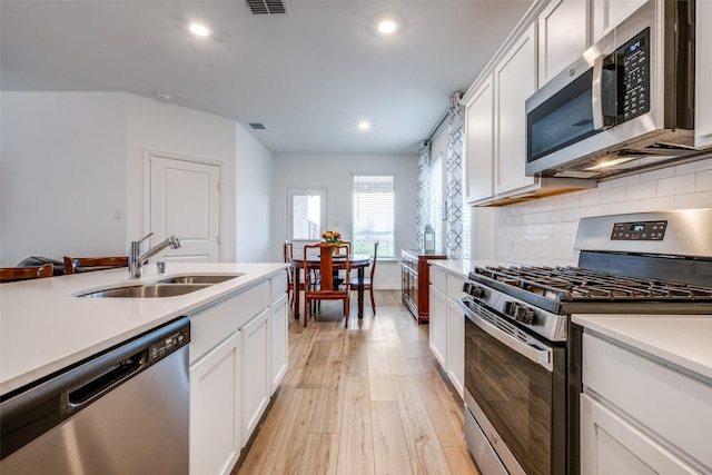 kitchen with light wood finished floors, tasteful backsplash, stainless steel appliances, light countertops, and a sink