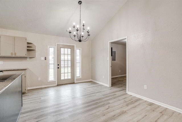 unfurnished dining area with an inviting chandelier, electric panel, vaulted ceiling, and light hardwood / wood-style flooring