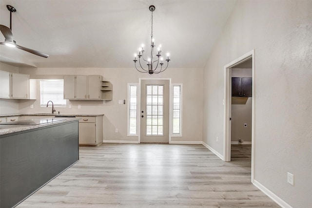 kitchen with light stone counters, hanging light fixtures, ceiling fan with notable chandelier, and light wood-type flooring