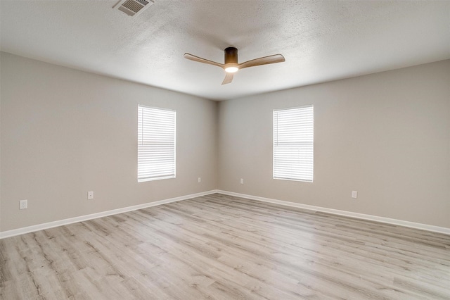 empty room with ceiling fan, plenty of natural light, a textured ceiling, and light hardwood / wood-style floors