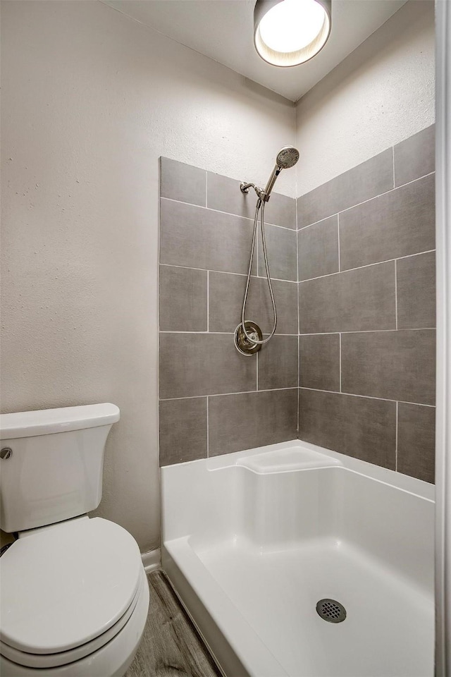 bathroom featuring hardwood / wood-style floors, a tile shower, and toilet