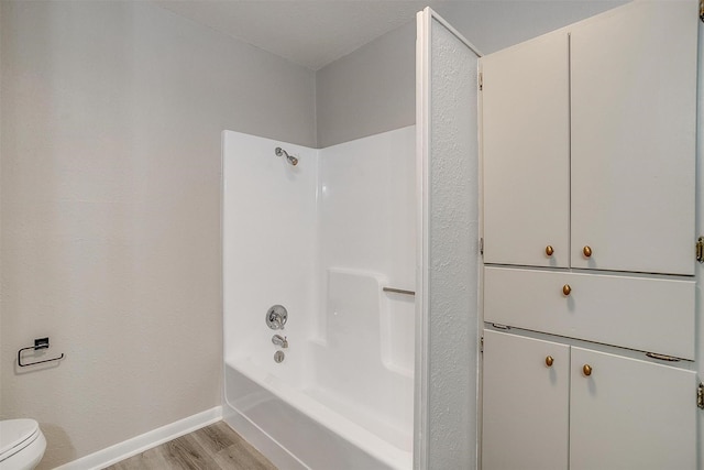 bathroom featuring wood-type flooring, tub / shower combination, and toilet