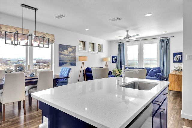 kitchen with an island with sink, sink, dark wood-type flooring, and decorative light fixtures