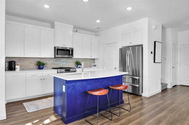 kitchen with sink, stainless steel appliances, white cabinets, a center island with sink, and decorative backsplash