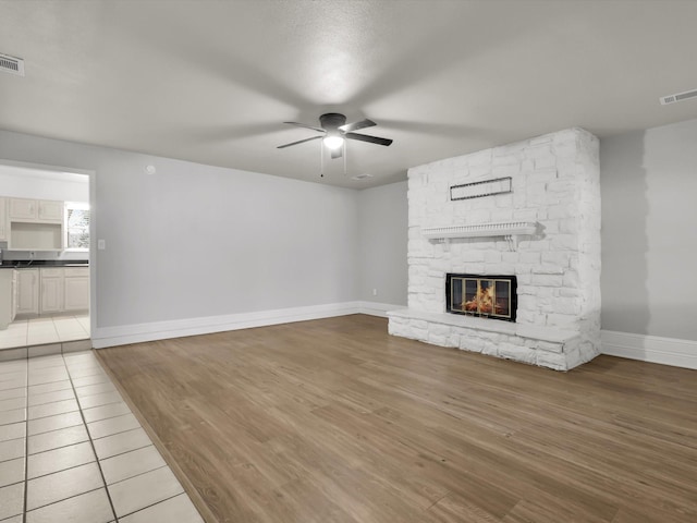 unfurnished living room with a stone fireplace, ceiling fan, and light hardwood / wood-style flooring