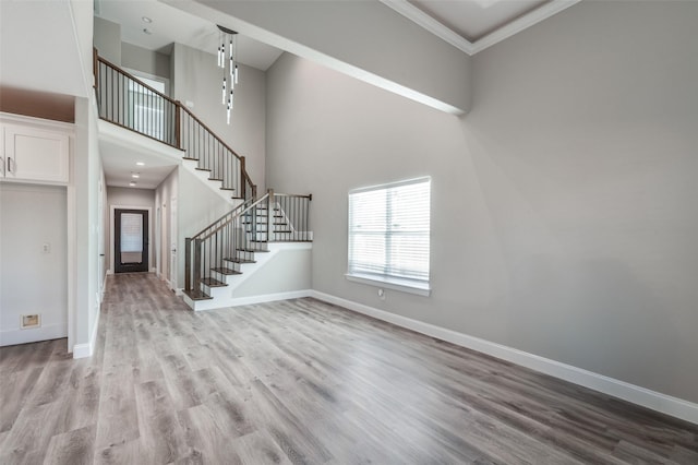 unfurnished living room with a towering ceiling, ornamental molding, and light hardwood / wood-style floors