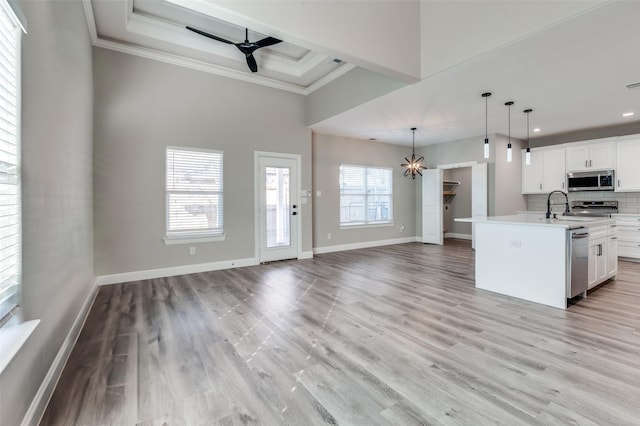 kitchen with appliances with stainless steel finishes, a raised ceiling, pendant lighting, a kitchen island with sink, and white cabinets