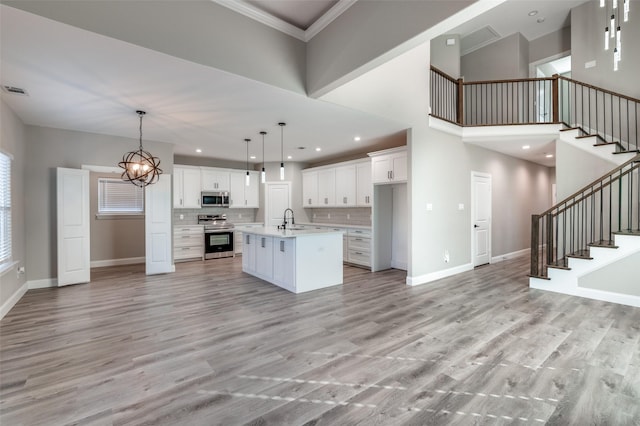 kitchen with sink, white cabinetry, hanging light fixtures, stainless steel appliances, and a kitchen island with sink