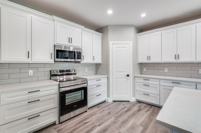 kitchen with appliances with stainless steel finishes, white cabinets, backsplash, and light hardwood / wood-style flooring