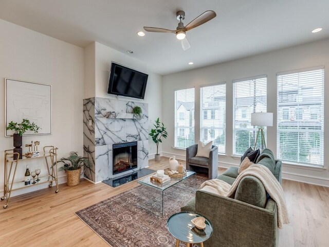 living room with ceiling fan, a healthy amount of sunlight, a premium fireplace, and wood-type flooring