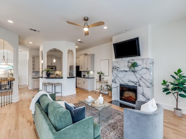 living room with ceiling fan, a high end fireplace, and light wood-type flooring