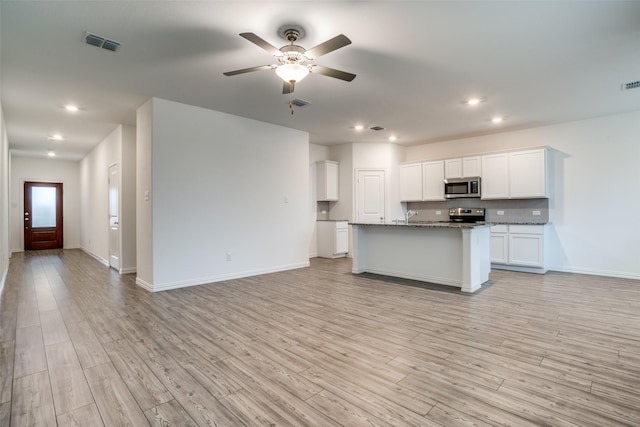 kitchen with light hardwood / wood-style flooring, a kitchen island with sink, white cabinetry, stainless steel appliances, and stone countertops