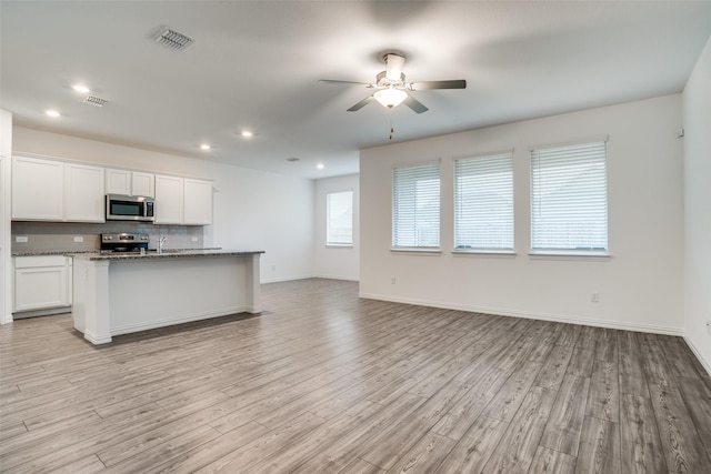 kitchen with stone counters, an island with sink, white cabinets, backsplash, and stainless steel appliances