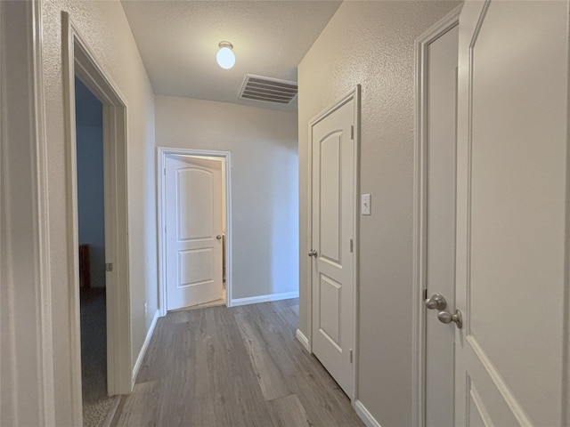 corridor with a textured ceiling and light wood-type flooring