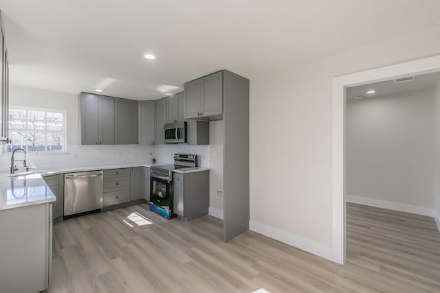 kitchen featuring sink, light hardwood / wood-style flooring, appliances with stainless steel finishes, gray cabinetry, and decorative backsplash