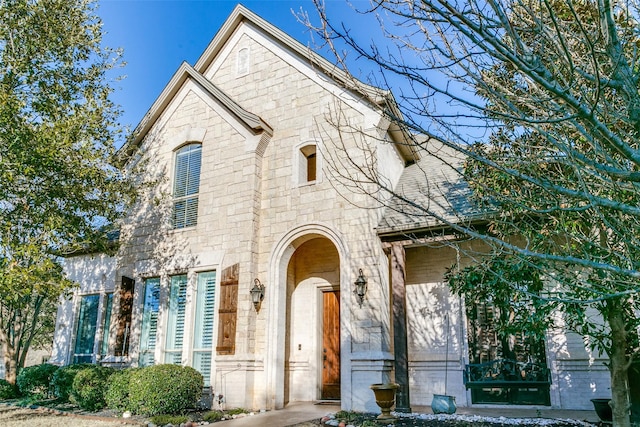 french country style house featuring stone siding, brick siding, and a shingled roof