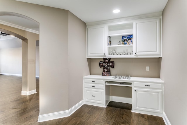 unfurnished office with dark wood-style floors, arched walkways, built in desk, and baseboards