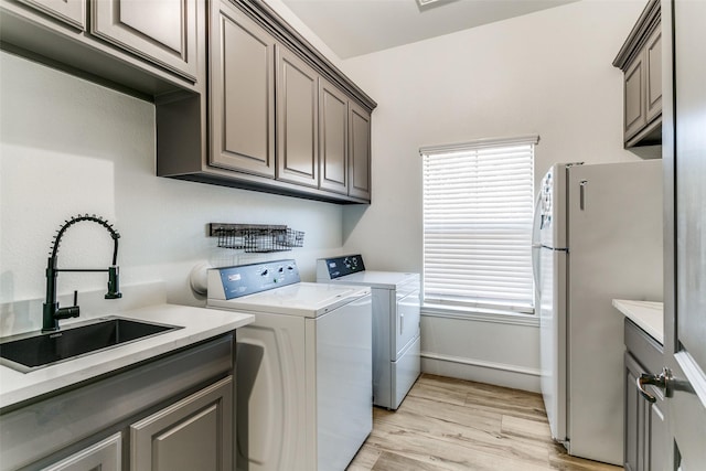 clothes washing area featuring washer and clothes dryer, a sink, cabinet space, and a healthy amount of sunlight