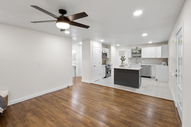 kitchen with white cabinetry, appliances with stainless steel finishes, a kitchen island, light hardwood / wood-style floors, and decorative backsplash