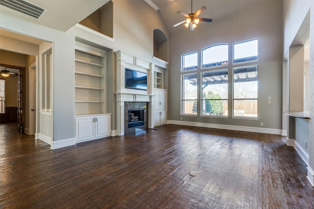 unfurnished living room with dark wood-type flooring, ceiling fan, a high ceiling, a fireplace, and built in shelves