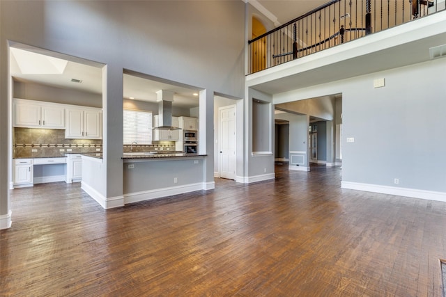 unfurnished living room with sink, a towering ceiling, dark wood-type flooring, and a skylight